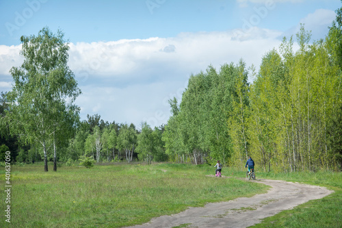 On a sunny summer day, brother and sister ride bicycles in the meadow along the road.