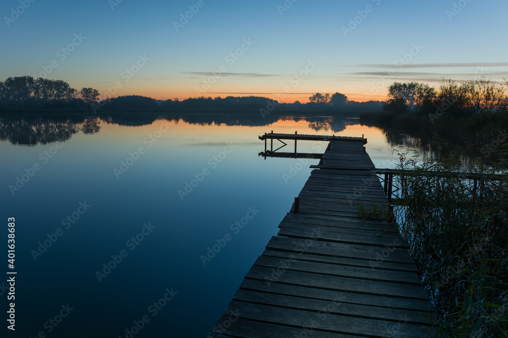 Wooden pier towards a calm lake and the sky after sunset