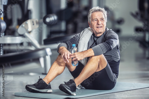 Older male rests with a bottle of water sitting on a mat during a gym workout