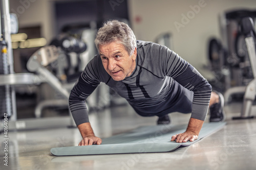 Senior male stays fit by doing pushups on a mat inside the fitness center