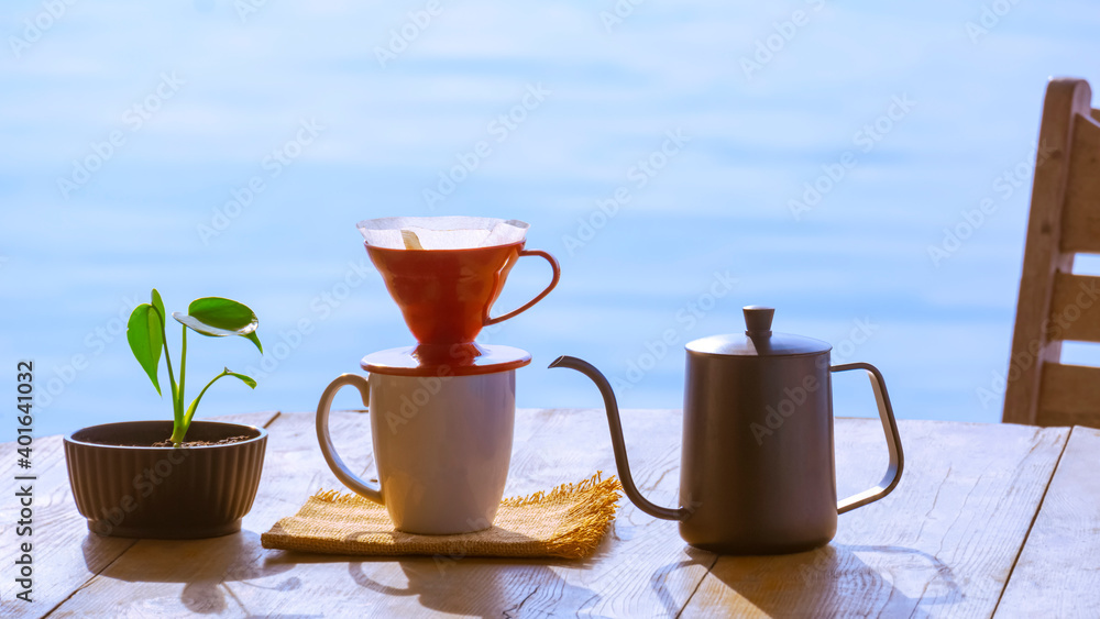 Drip coffee cup set with green plant in flower pot on wooden round table against riverside view background at morning time