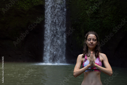 Fototapeta Naklejka Na Ścianę i Meble -  Close up of namaste mudra. Woman meditating, practicing yoga and pranayama with namaste mudra near waterfall. Yoga outdoor concept. Tibumana waterfall, Bali. Copy space.