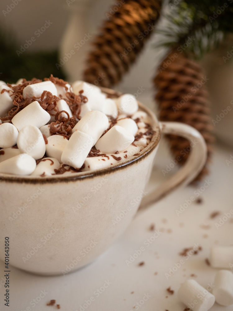 A cup of cocoa with marshmallows on the background of fir branches with cones in a vase and a burning candle on a light background in the morning light A cup of cocoa with marshmallows on the background of fir branches with cones in a vase and a burning candle on a light background in the morning light