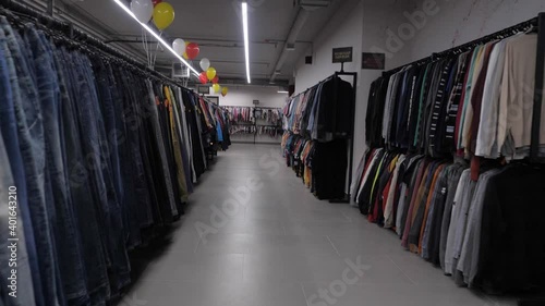 A clothing store without people. Lots of clothes on hangers. Jeans, sweaters, T-shirts. Second hand shop. Slow motion along the rows of clothes.