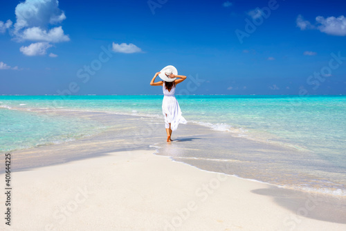 A woman in a white summer dress stands on a sandbar surrounded by turquoise ocean in the Maldives islands