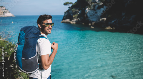 South Asian hipster guy wanderlust with rucksack enjoying summer vacations for explore wild nature at coastline, Indian male enjoying travel active recreating during solo holidays on Balearic islands