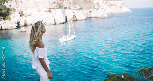 Carefree female tourist breathing freedom during summer vacations in Spanish resort with Mediterranean coastline, youthful traveler in white clothing enjoying picturesque views of Menorca island photo