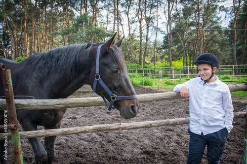 In summer, on a bright sunny day, a boy stands next to a horse on a ranch.