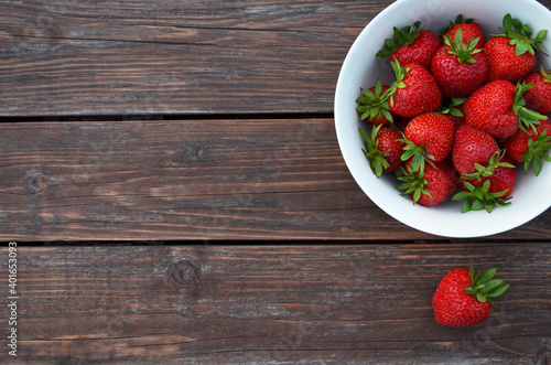 Fresh red strawberries in a white bowl on a old wooden table close-up with copy space, top view. Healthy eating concept.