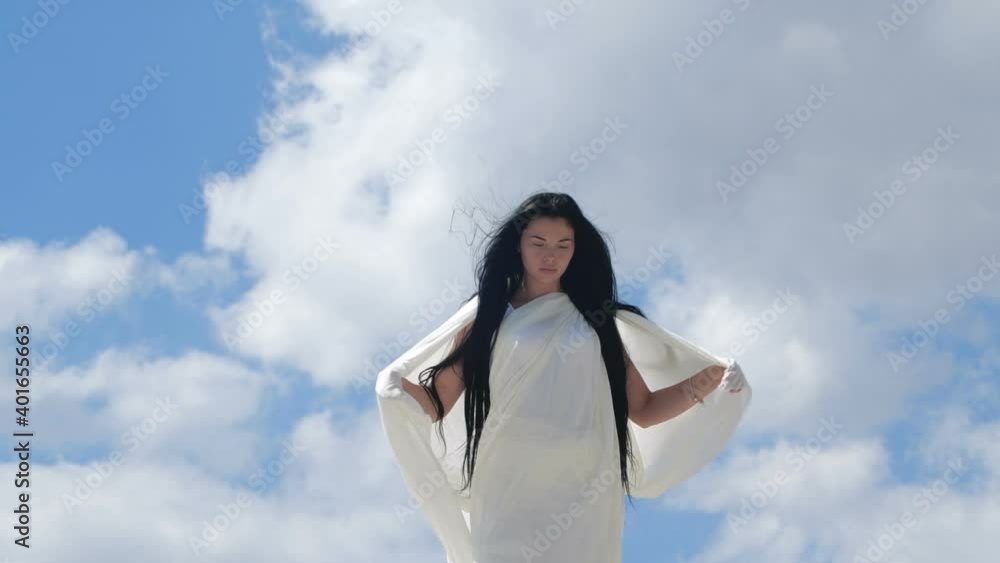 A beautiful brunette woman with long hair stands on the top of a hill against the sky in white fluttering clothes. Mirage of angelic being. 200 fps slow motion A beautiful brunette woman with long hair stands on the top of a hill against the sky in white fluttering clothes. Mirage of angelic being. 200 fps slow motion