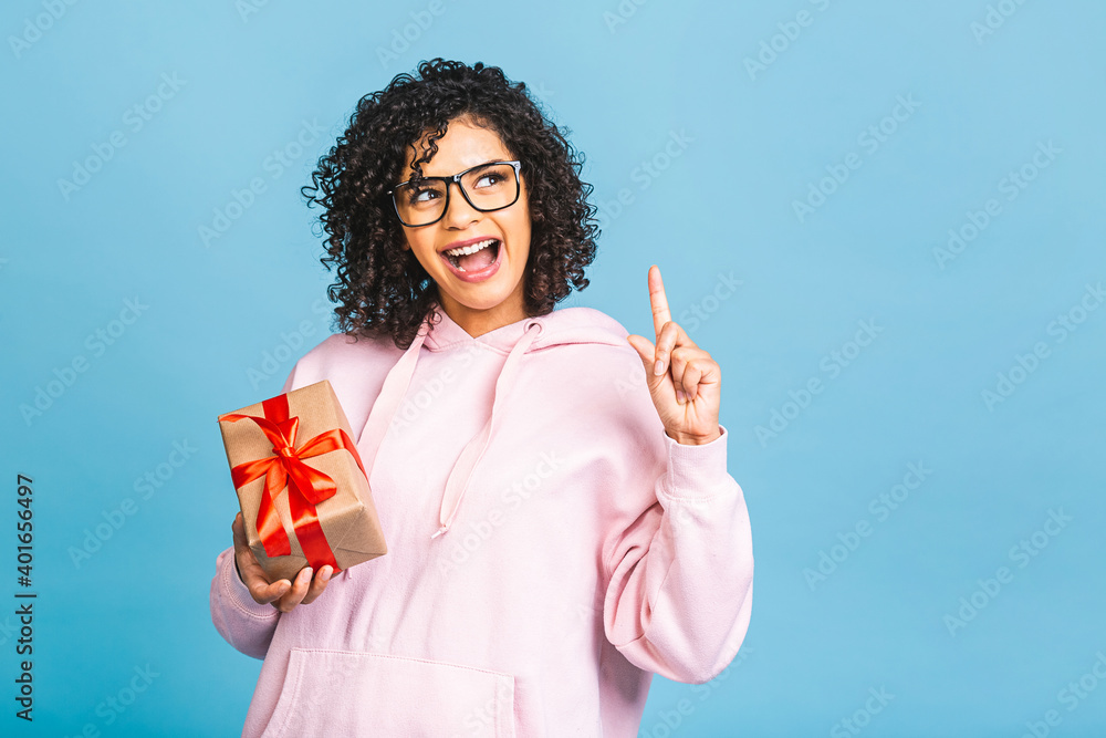 Happy african american curly lady in casual laughing while holding present gift box isolated over blue background. Happy african american curly lady in casual laughing while holding present gift box isolated over blue background.