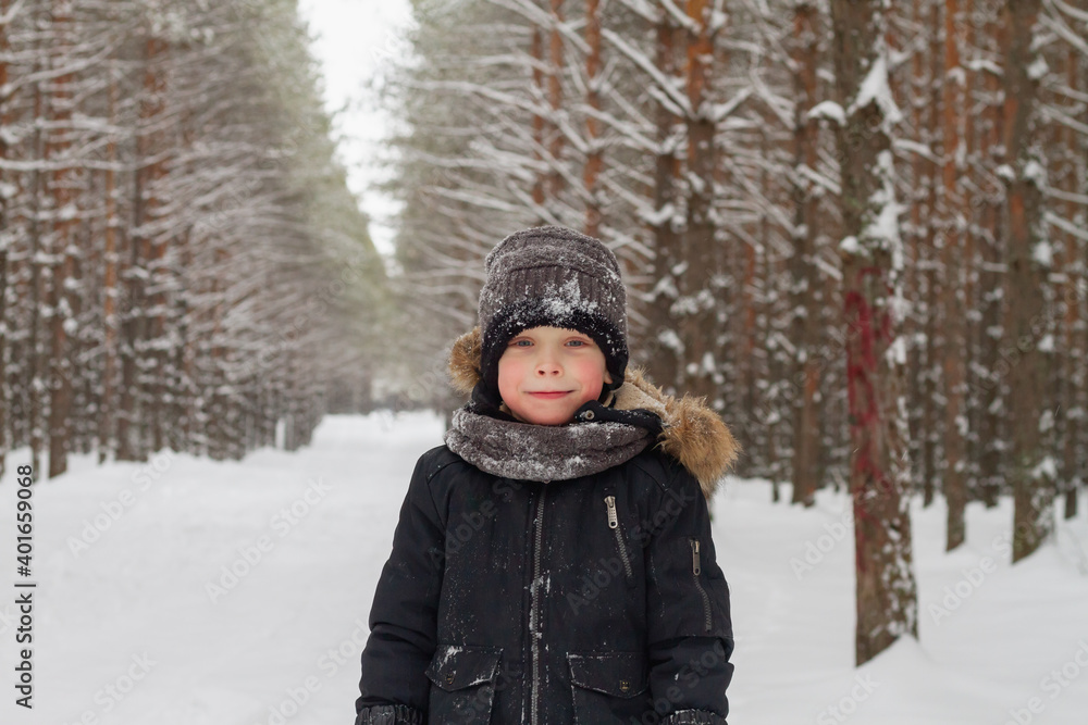 European boy in the forest in a hat in winter on the background of snow.