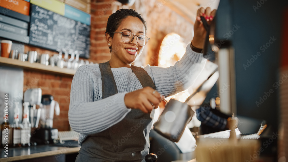 © Gorodenkoff - Beautiful Latin American Female Barista with Short Hair and Glasses is Making a Cup of Tasty Cappuccino in Coffee Shop Bar. Male Cashier Works at a Cozy Loft-Style Cafe Counter in the Background.