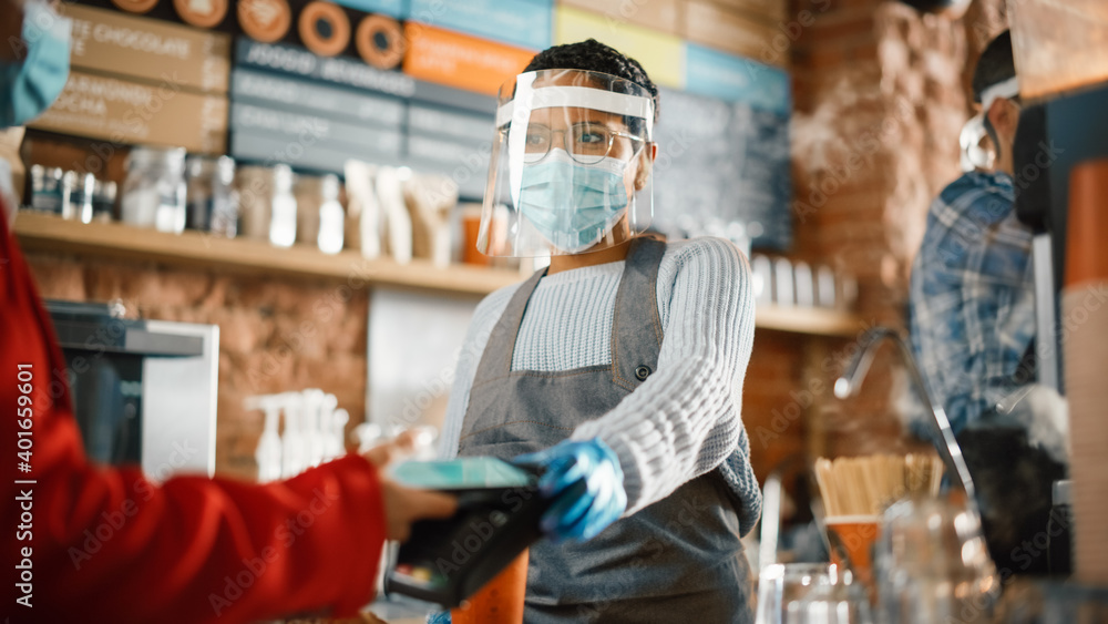 Mandatory Face Masks and Shields in a Coffee Shop During Coronavirus Pandemic. Female Customer Pays for Coffee and Pastry with Contactless NFC Payment Technology on Smartphone to a Barista in Cafe.