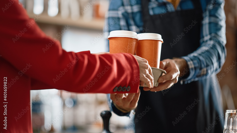 © Gorodenkoff - Shot in Modern in Cafe: Handsome Barista in Checkered Shirt Passes Two Cups of Take Away Coffee to a Young Female Customer in Red Coat. Close-up Shot with Focus on Hands.