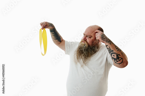 An overweigh man mysteriously lookings at a fitness band while thinking how to use it. Emotion. photo