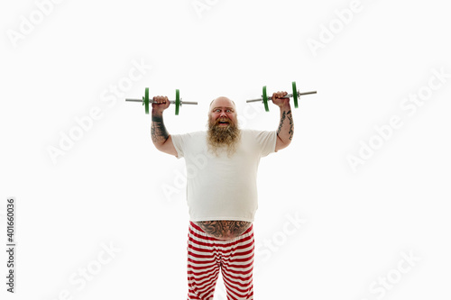 Isolated portrait of an overweigh bearded man with tattooed arms exercising with dumbbells and having fun looking at camera