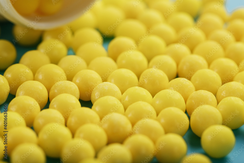 Yellow vitamin C capsules spilled out of a white jar against a blue background. Yellow vitamin C capsules spilled out of a white jar against a blue background.