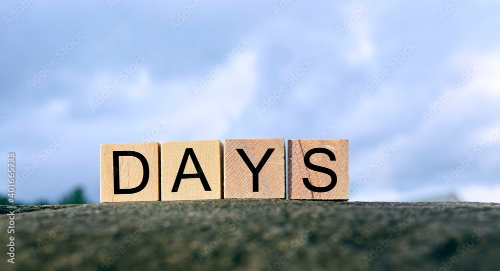 Fototapeta premium Days text on wooden block on top of big stone with blurred sky background