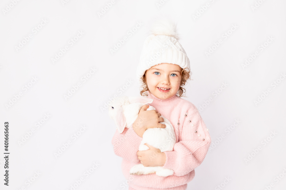 a little girl in winter clothes holds a rabbit on a white background. New year's concept, space for text a little girl in winter clothes holds a rabbit on a white background. New year's concept, space for text