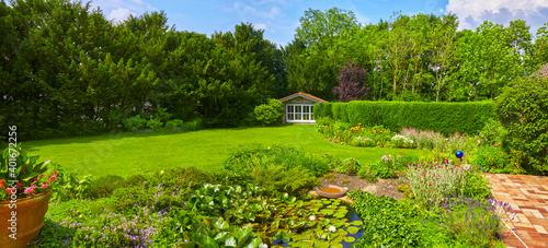 Fototapeta Naklejka Na Ścianę i Meble -  Well-kept garden with a colorful flower bed, garden shed and pond.