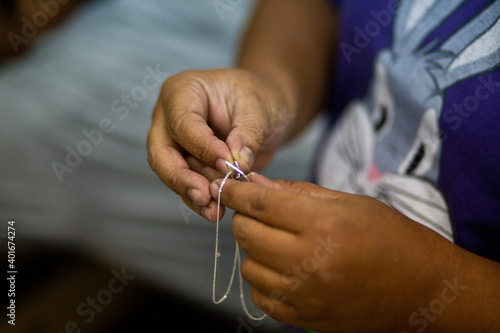 close hands of the master with silver chains. Manual jewelry production