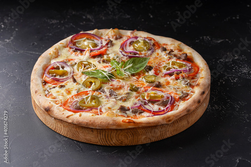 Pizza with meat cheese onion jalapeno on a dark background.