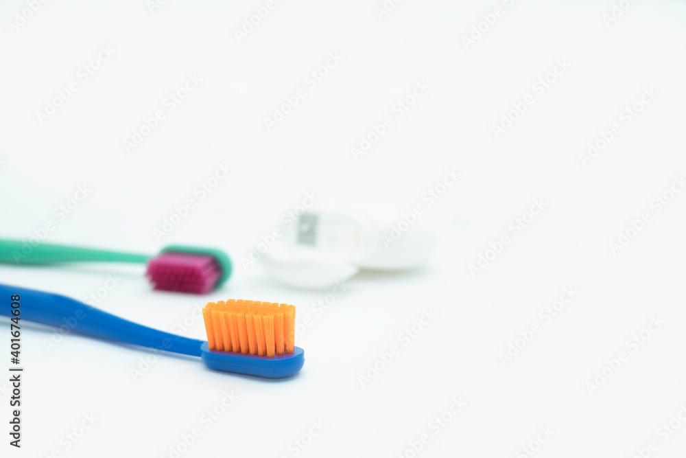 Two colored toothbrushes with bright orange and red bristles and dental floss lie on a white background, daily oral care
