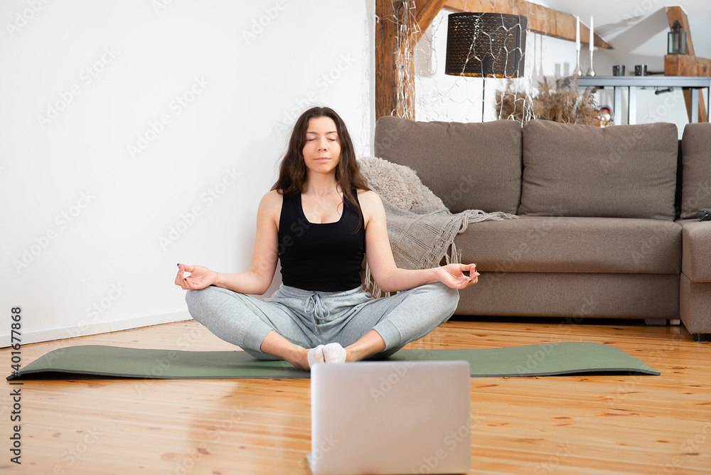 Yoga online. Relaxed young woman meditating front of laptop at home, sitting in lotus position Yoga online. Relaxed young woman meditating front of laptop at home, sitting in lotus position