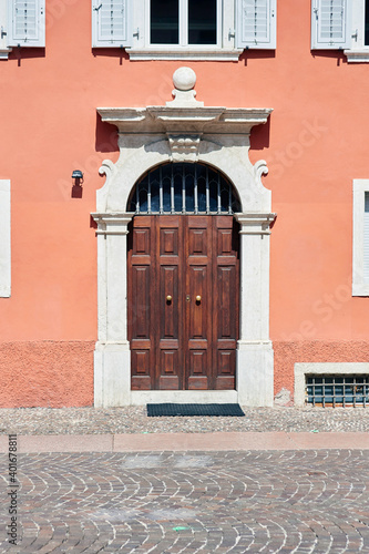 Italian retro wood style front door, the main entrance on the red color wall facade. Element of the classic Italian facade and architecture