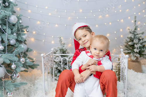 two beautiful brothers in Christmas costumes are sitting by the fence and hugging. friendship of brothers, support, family, holiday, postcard