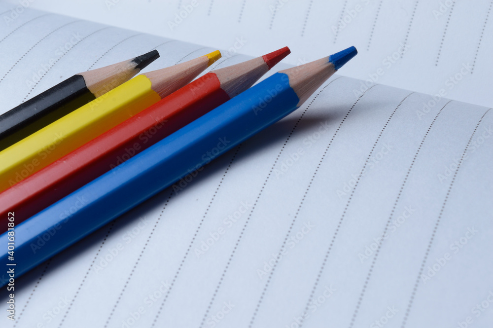 four multi-colored pencils - blue, red, yellow, black. lie on an open notebook. four multi-colored pencils - blue, red, yellow, black. lie on an open notebook.