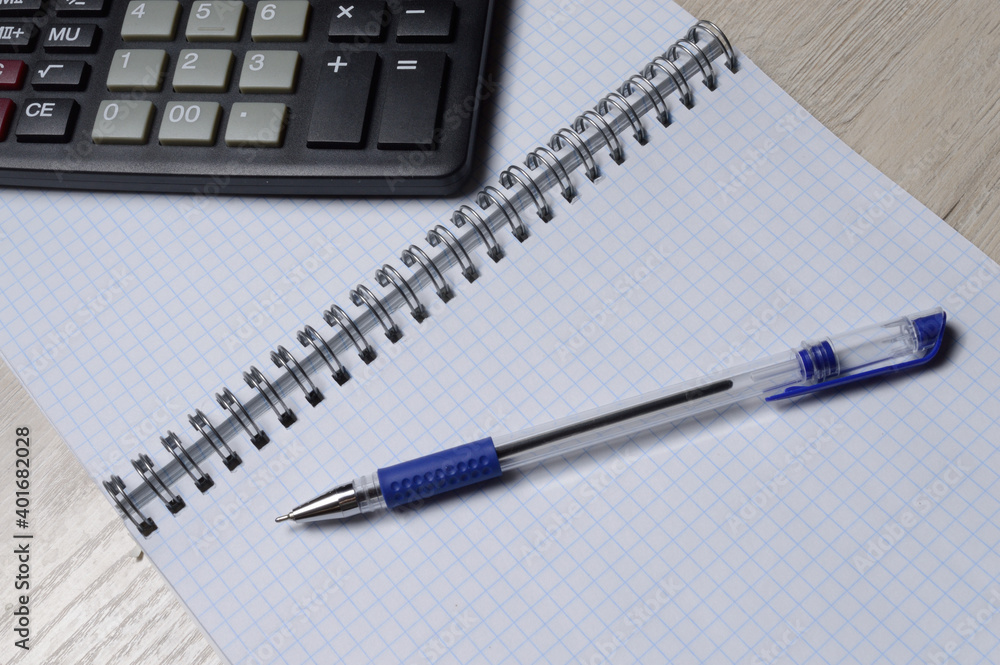 a ballpoint pen and a micro calculator lie on a squared notebook. close-up. a ballpoint pen and a micro calculator lie on a squared notebook. close-up.
