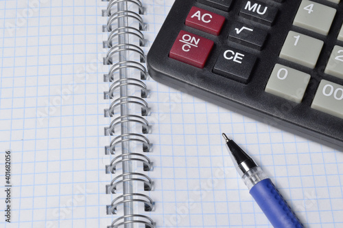 a ballpoint pen and a micro calculator lie on a squared notebook. close-up.