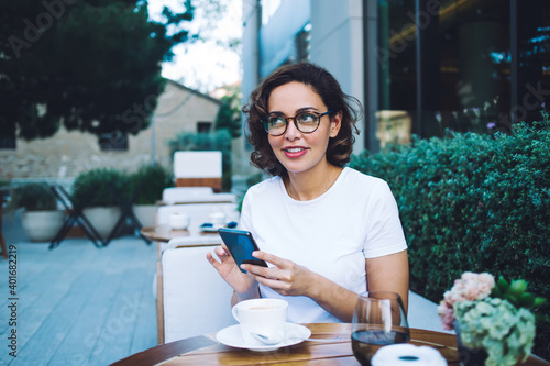 Glad woman with smartphone resting in outdoor cafeteria