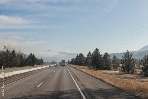 An asphalt road along which cars and trucks go, among the mountains, ahead on the horizon mountains in fog, the sky is covered with clouds. Idaho, USA, 11-23-2019 © Liudmila