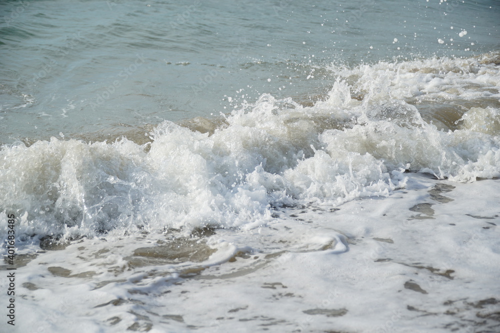 Ocean waves splashing onto the shore of a sandy beach causing white foam and bubbles Ocean waves splashing onto the shore of a sandy beach causing white foam and bubbles