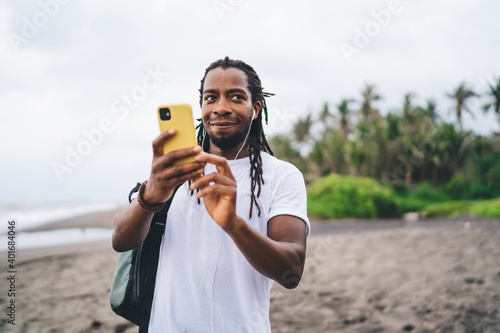 Cheerful black man surfing cellphone on tropical coastline