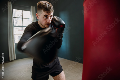 A young athletic man is hitting a boxing bag. Boxer practicing punches in the ring. The athlete strikes with a punching bag. © Chiheisen