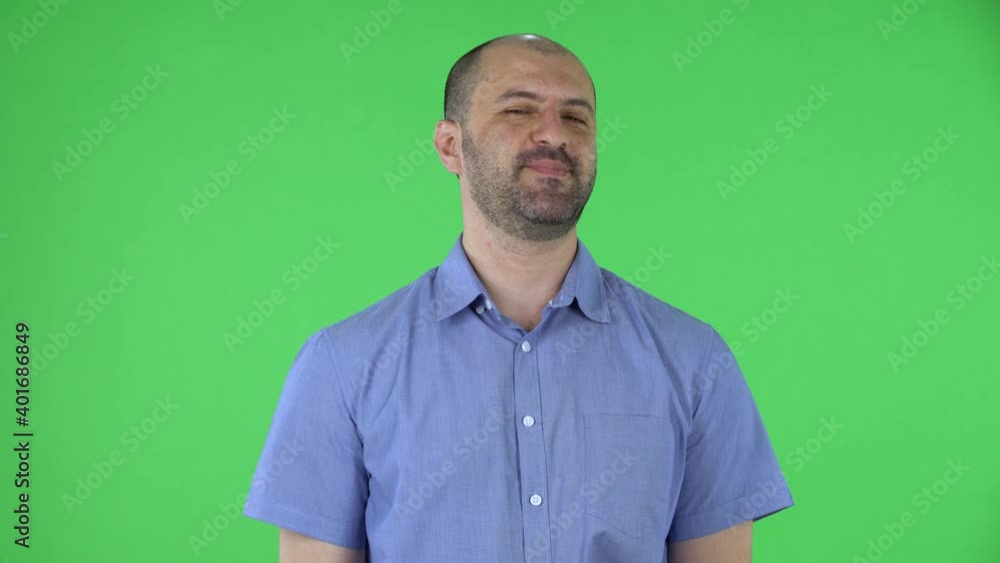Portrait of a middle aged men playfully looking at the camera and making a heart gesture and blowing a kiss. Balding male with beard in blue shirt posing on green screen in the studio. Close up. Portrait of a middle aged men playfully looking at the camera and making a heart gesture and blowing a kiss. Balding male with beard in blue shirt posing on green screen in the studio. Close up.