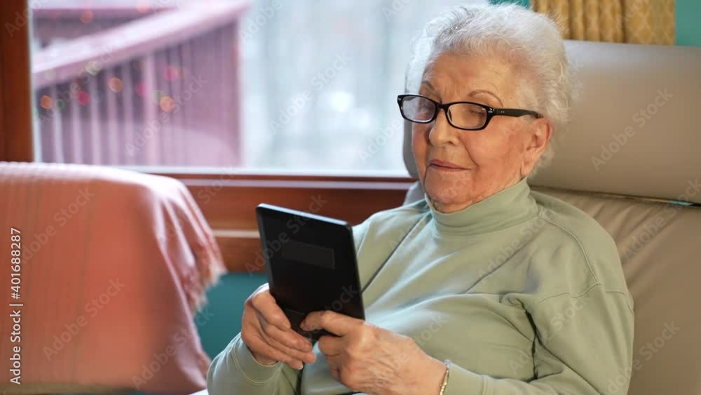 Extreme closeup elderly woman relaxing holding digital tablet reading e book sit in recliner chair at home, senior adult lady enjoying using computer pad apps browsing internet shopping in living room Extreme closeup elderly woman relaxing holding digital tablet reading e book sit in recliner chair at home, senior adult lady enjoying using computer pad apps browsing internet shopping in living room