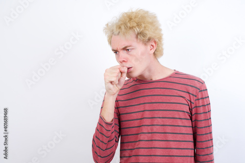 Young handsome Caucasian blond man standing against white background feeling unwell and coughing as symptom for cold or bronchitis. Healthcare concept.