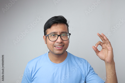 a young indian man in spectacles looking towards the camera and smiling with clean teeth and showing a fantastic hand gesture sign