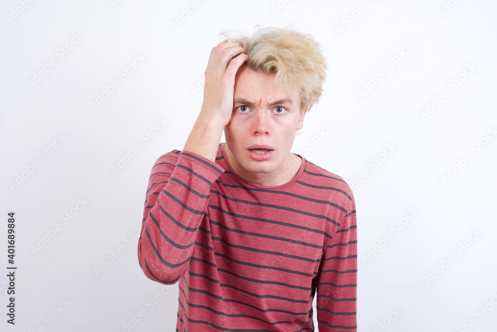 Embarrassed Young handsome Caucasian blond man standing against white background with shocked expression, expresses great amazement, Puzzled model poses indoor Embarrassed Young handsome Caucasian blond man standing against white background with shocked expression, expresses great amazement, Puzzled model poses indoor