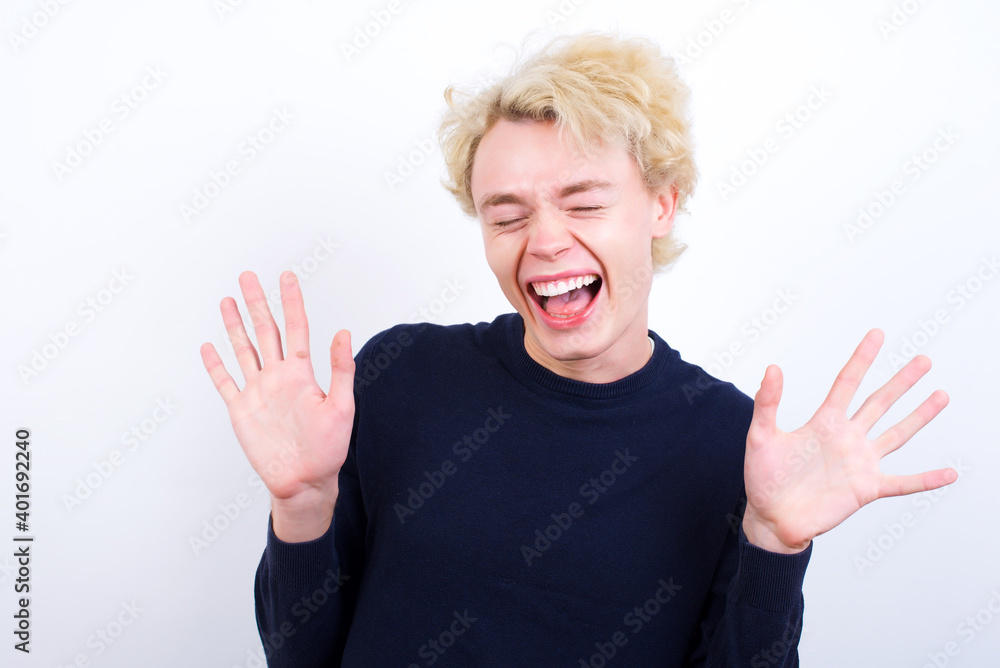 Emotive Young handsome Caucasian blond man standing against white background laughs loudly, hears funny joke or story, raises palms with satisfaction, being overjoyed amused by friend Emotive Young handsome Caucasian blond man standing against white background laughs loudly, hears funny joke or story, raises palms with satisfaction, being overjoyed amused by friend