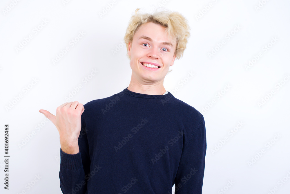Lovely Young handsome Caucasian blond man standing against white background pointing aside with forefinger, showing at copy space having news about bargains Lovely Young handsome Caucasian blond man standing against white background pointing aside with forefinger, showing at copy space having news about bargains