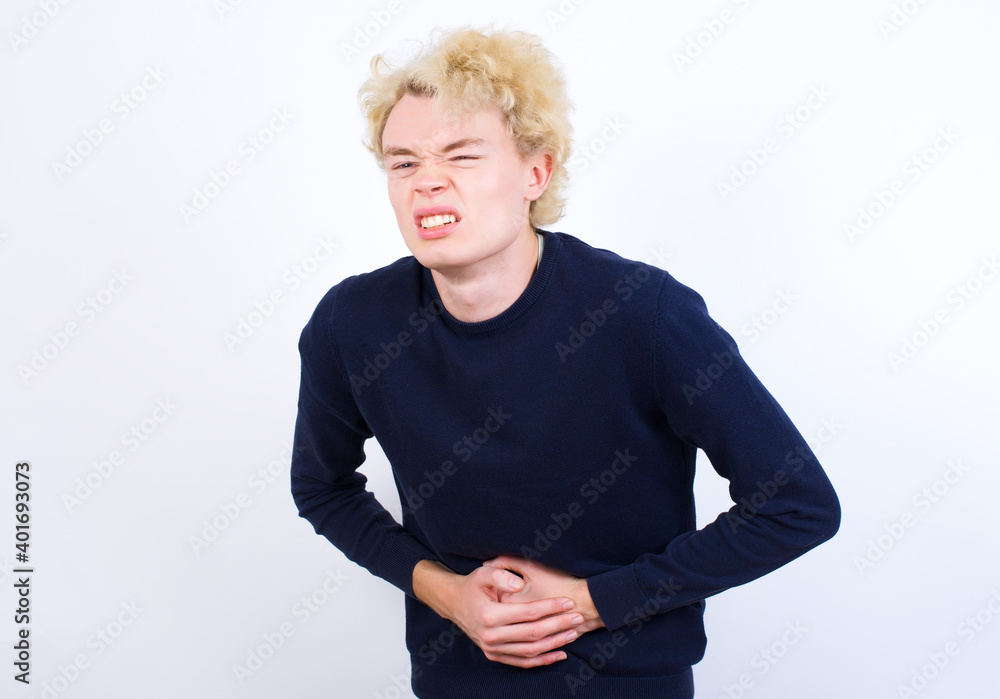 Young handsome Caucasian blond man standing against white background with hand on stomach because nausea, painful disease feeling unwell. Ache concept. Young handsome Caucasian blond man standing against white background with hand on stomach because nausea, painful disease feeling unwell. Ache concept.