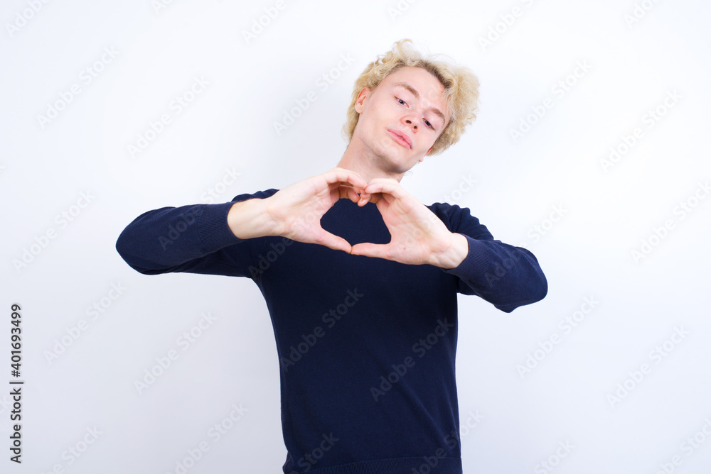 Fototapeta premium Young handsome Caucasian blond man standing against white background smiling in love doing heart symbol shape with hands. Romantic concept.