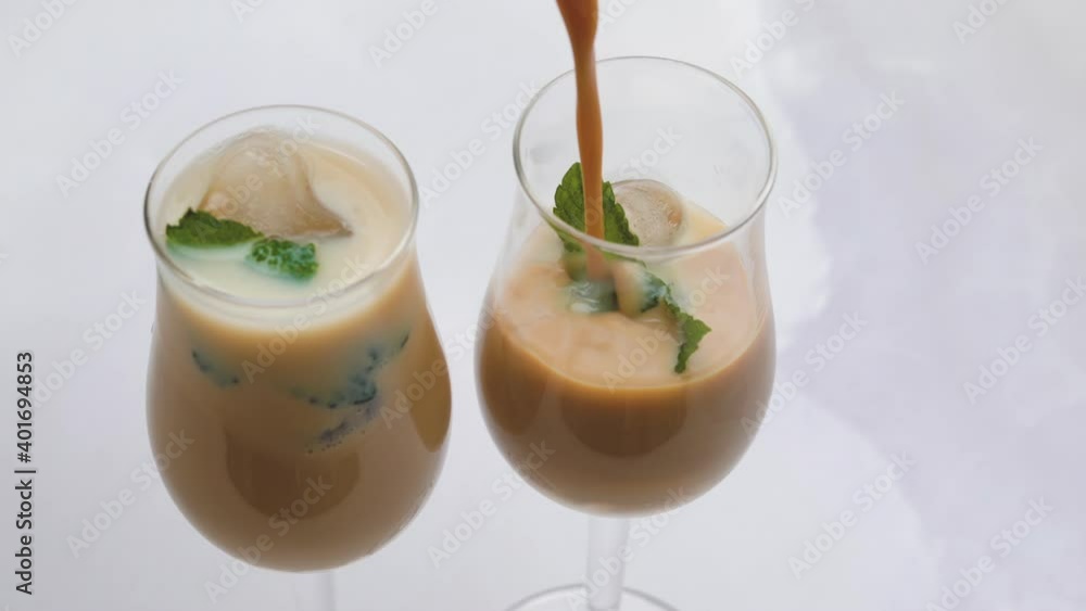 Cream liquor with frozen ice mint leaves close up in glasses on light background. Pouring liquor into glasses Cream liquor with frozen ice mint leaves close up in glasses on light background. Pouring liquor into glasses