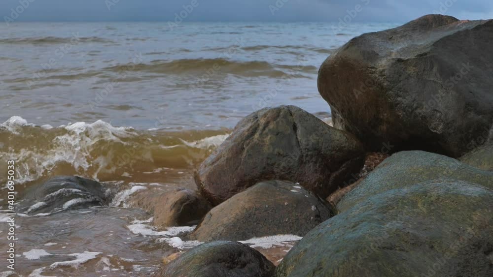 The sea waves wash away the big stones. Rain clouds are visible in the sky The sea waves wash away the big stones. Rain clouds are visible in the sky